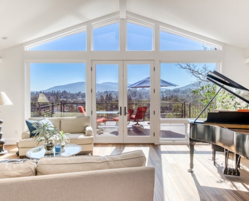 A cozy living room with a grand piano and large windows offering breathtaking views of the mountains.