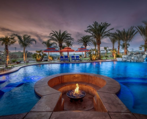 A serene pool surrounded by lounge chairs and a fire pit, creating a perfect ambiance for relaxation and enjoyment.